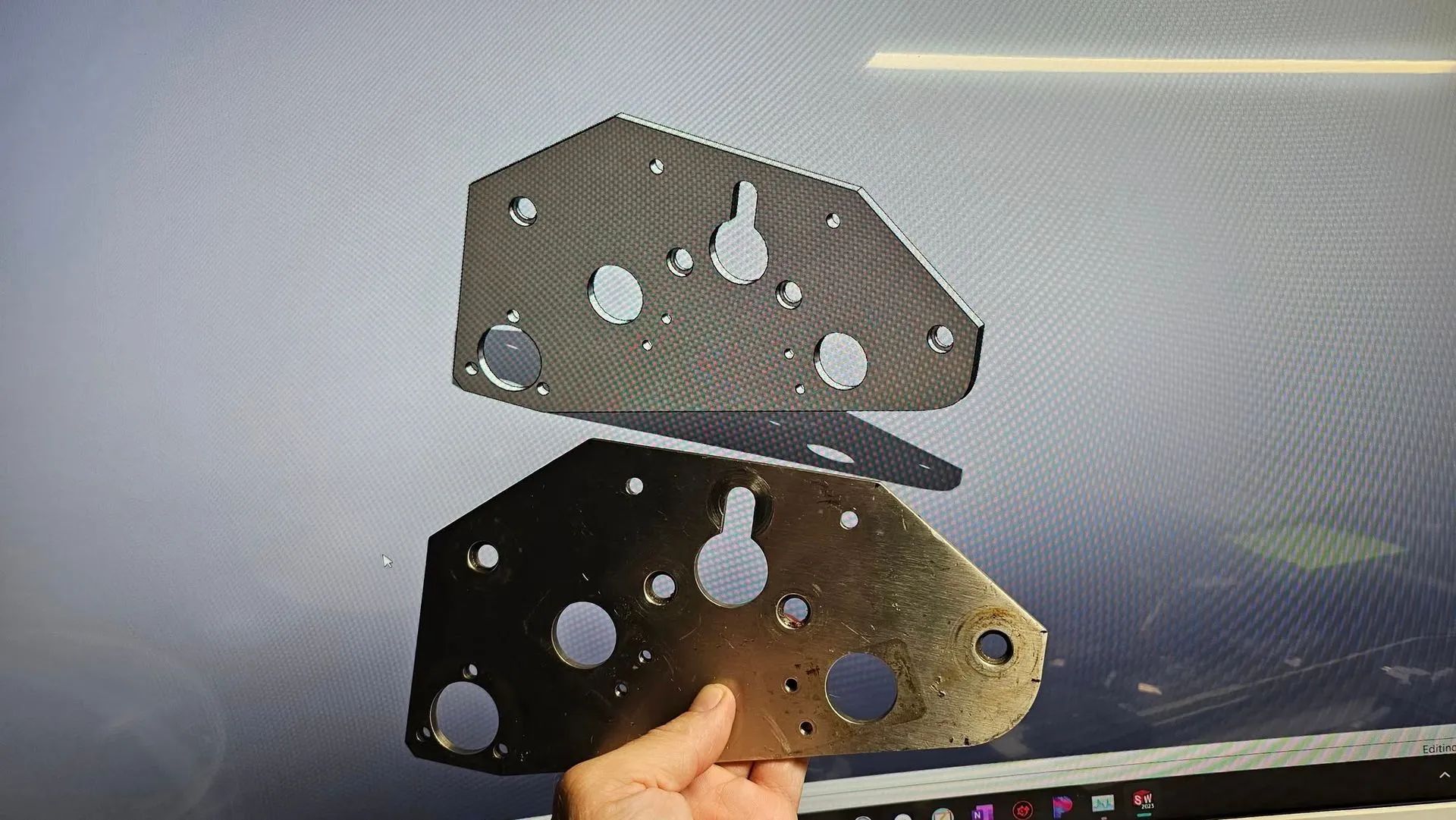 Hand holding two metal plates with multiple cutout holes, one silver and one black, against a light background