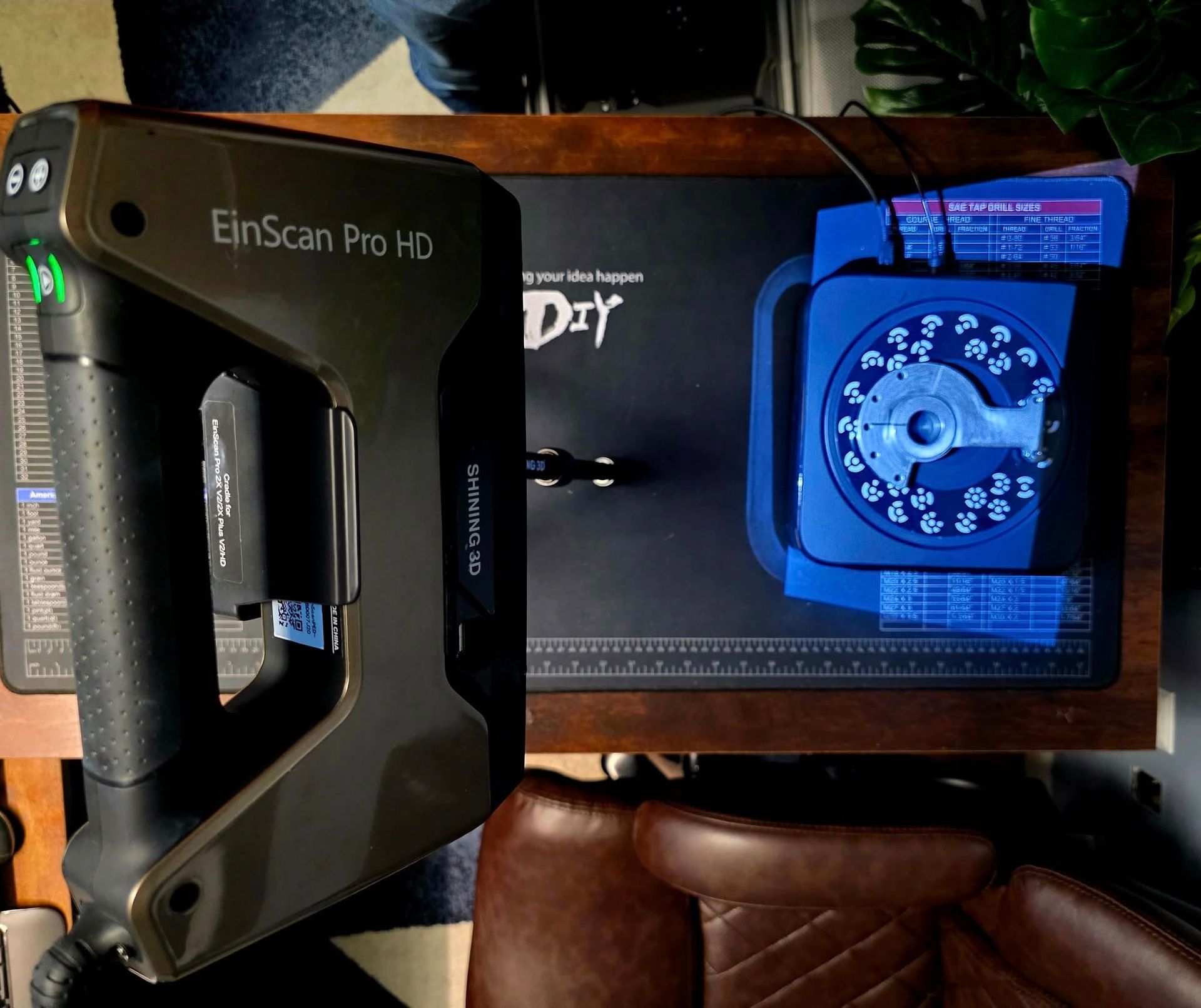 A dark-colored 3D scanner and blue turntable on a wooden surface for DIY projects.