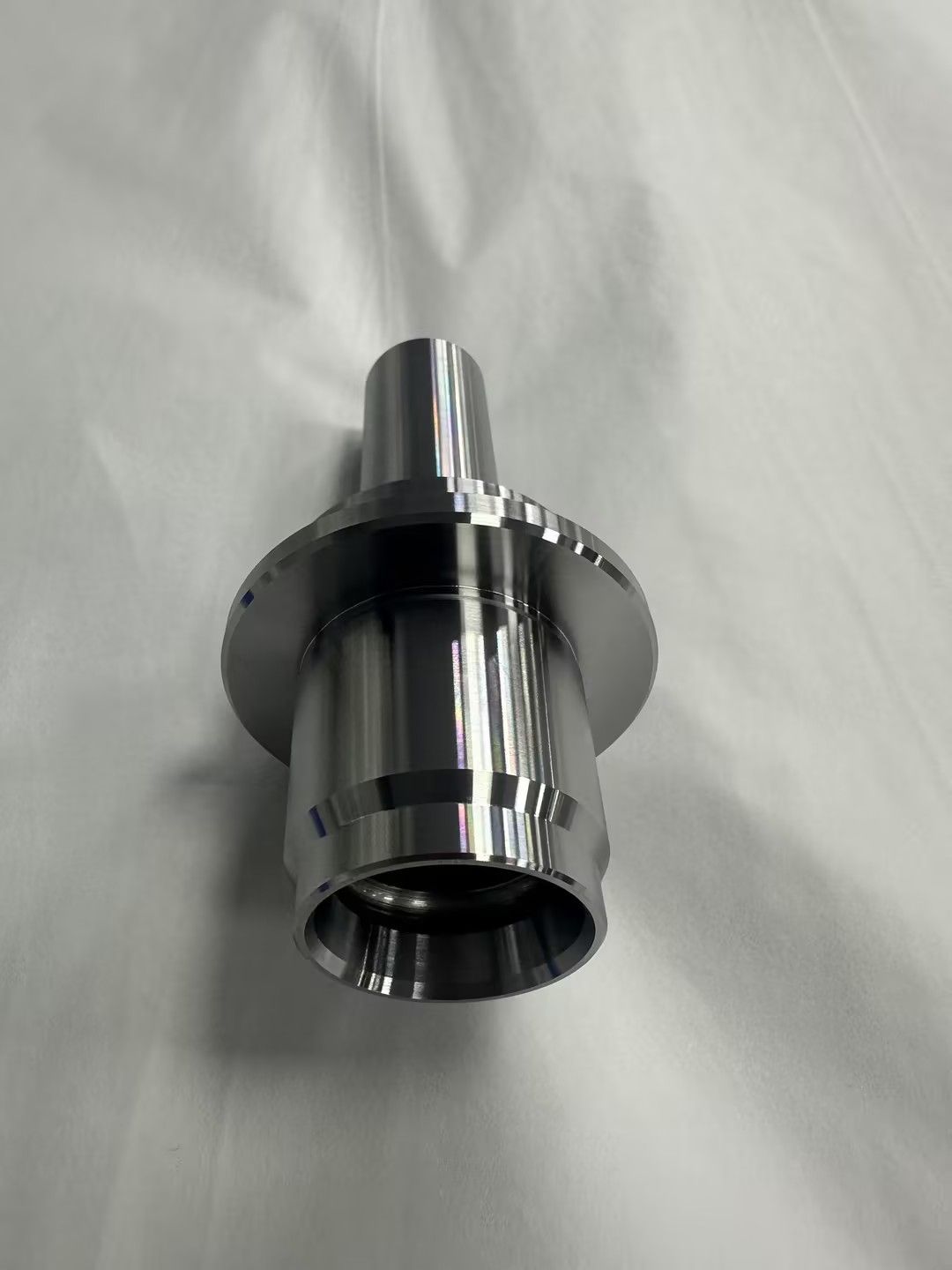 Metallic cylindrical hardware part with a flanged rim, lying on a white surface
