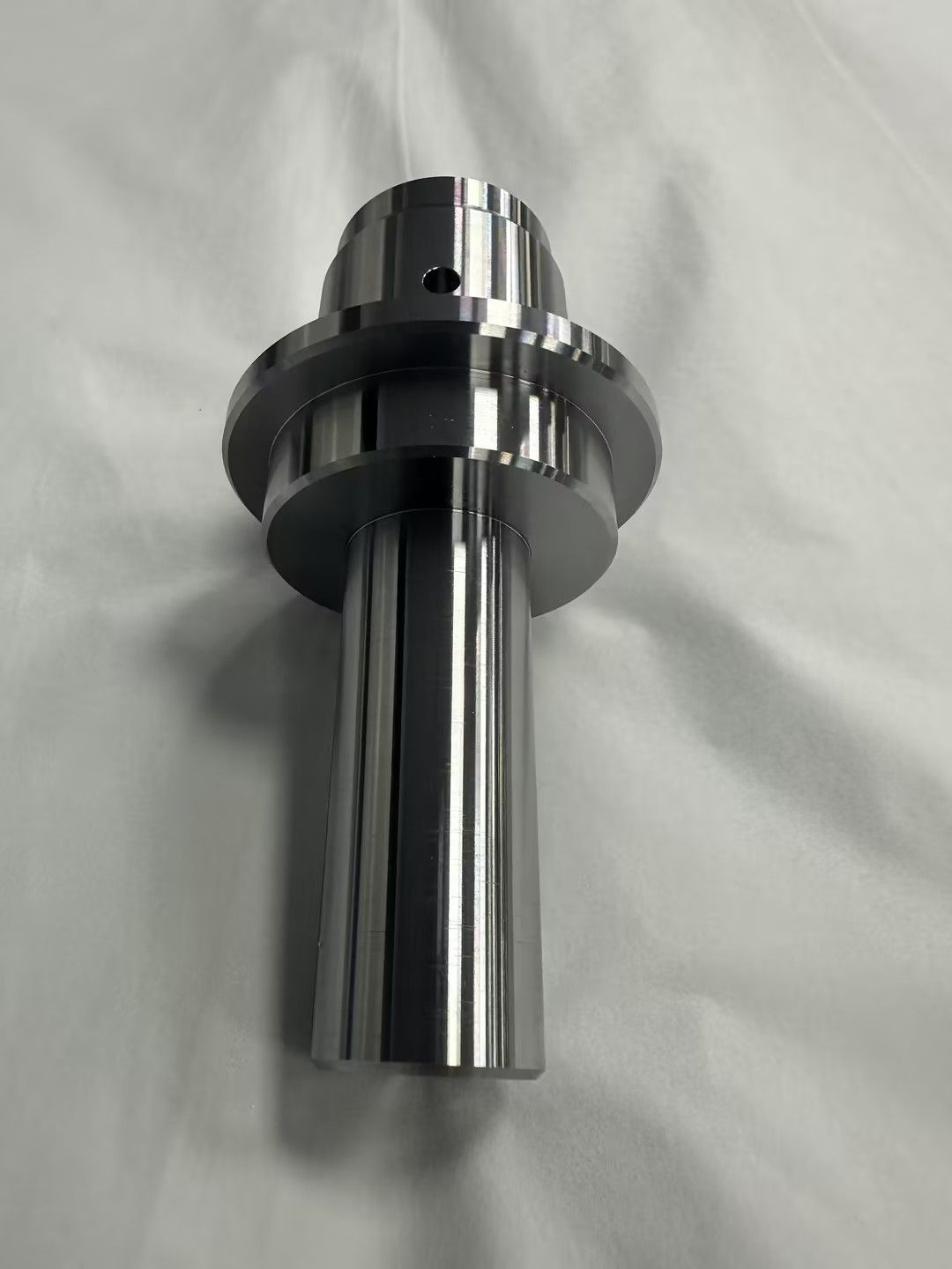 Shiny chrome metal machined part with a flanged top, shown on a white surface