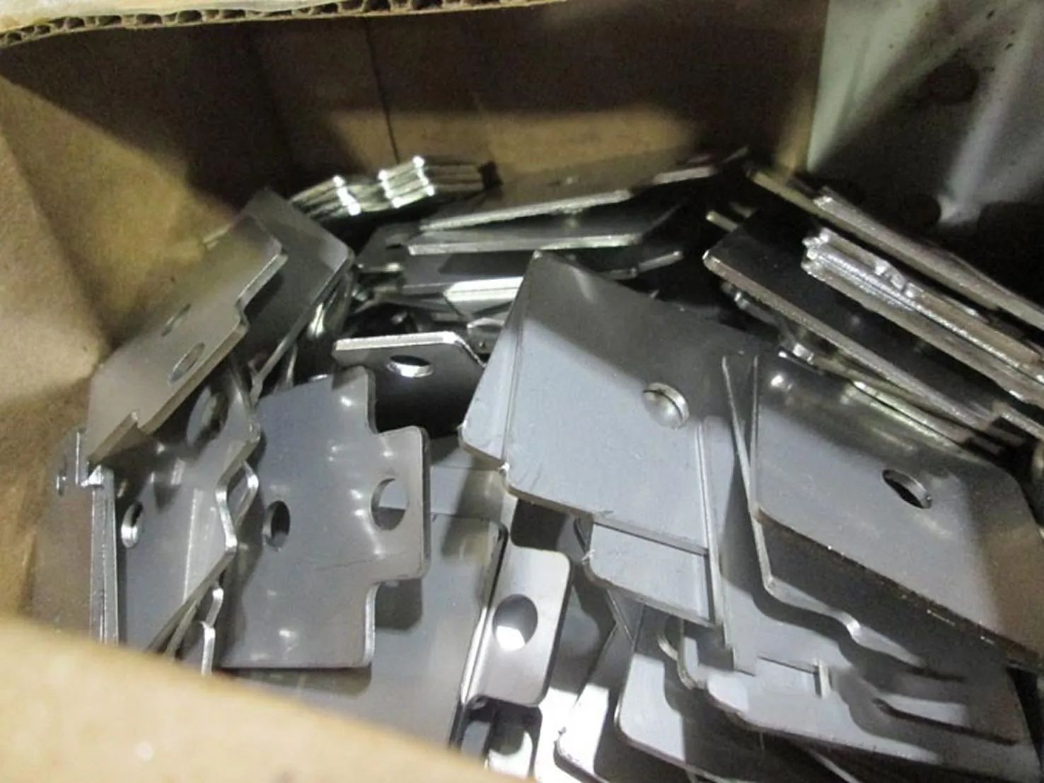 Box filled with stacked metal brackets and hardware parts