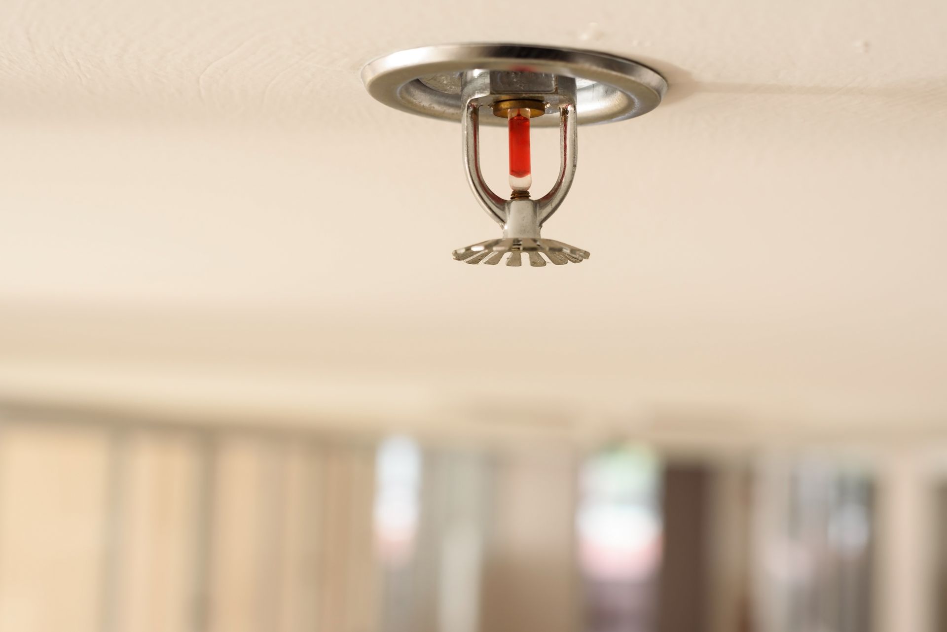 Ceiling-mounted fire sprinkler with red glass bulb on a white ceiling, blurred room background Ceiling-mounted fire sprinkler with red glass bulb on a white ceiling, blurred room background