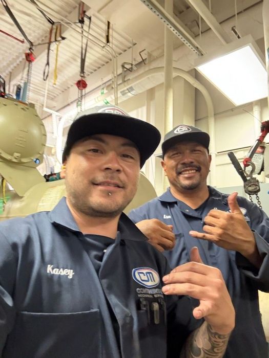 Three workers in blue uniforms repairing an outdoor air conditioner unit by a brick wall Three workers in blue uniforms repairing an outdoor air conditioner unit by a brick wall
