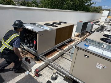 Two technicians in hard hats repair a rooftop HVAC unit with tools. Two technicians in hard hats repair a rooftop HVAC unit with tools.