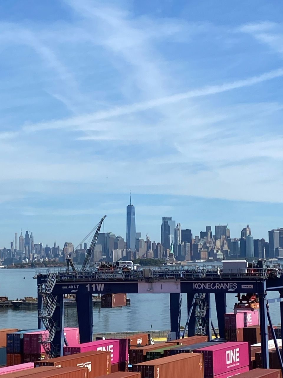 City skyline across the water under a blue sky, with a ferry dock and a crane in the foreground