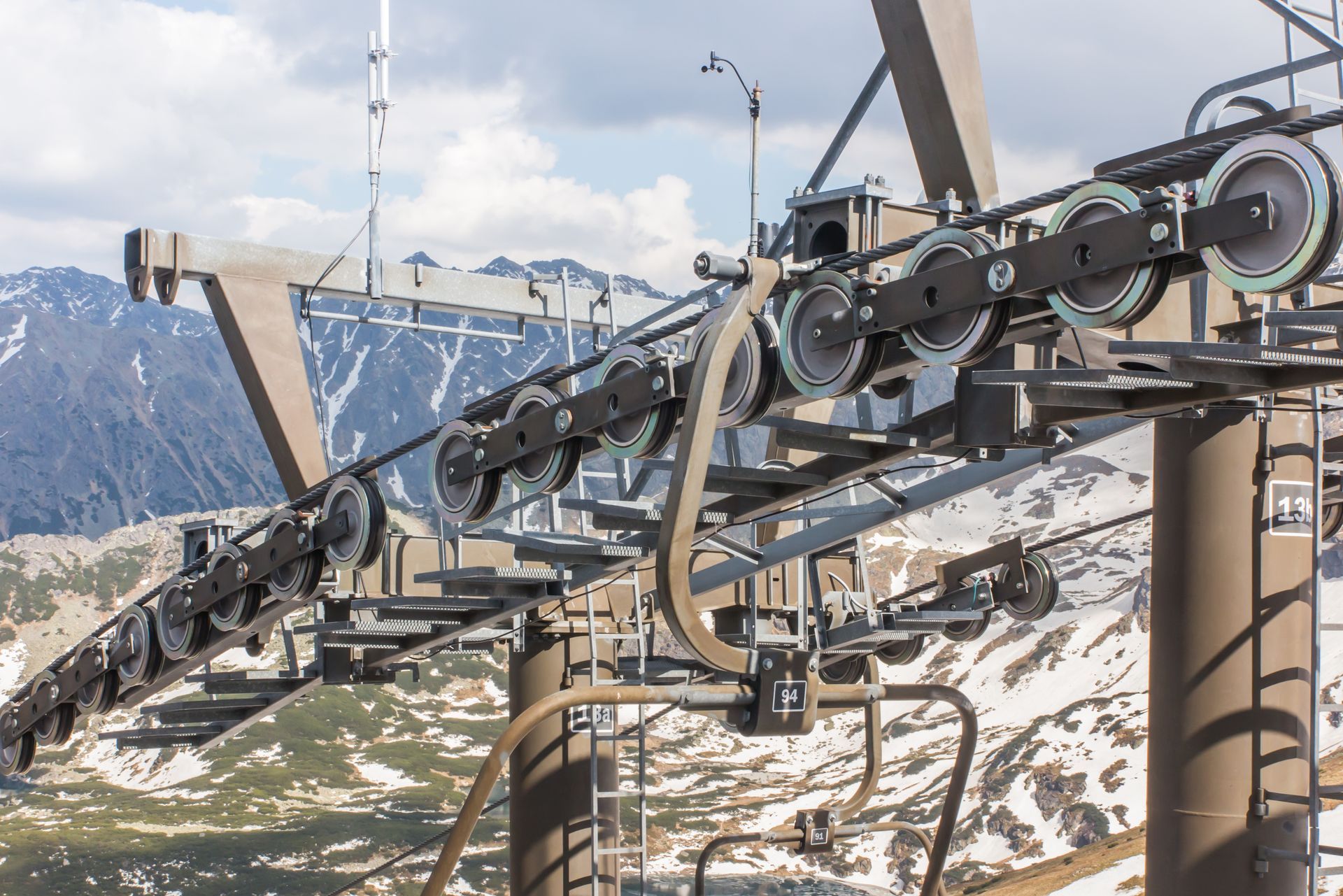 Chairlift machinery with cables over a snowy mountain slope and peaks