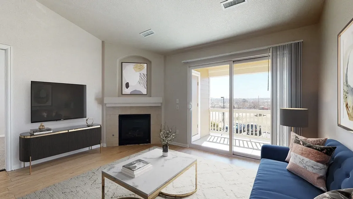 Modern living room with fireplace, TV, blue sofa, coffee table, and balcony doors overlooking a bright view