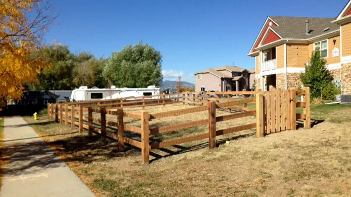 Wooden fenced yard beside a sidewalk and brick townhouse on a sunny day