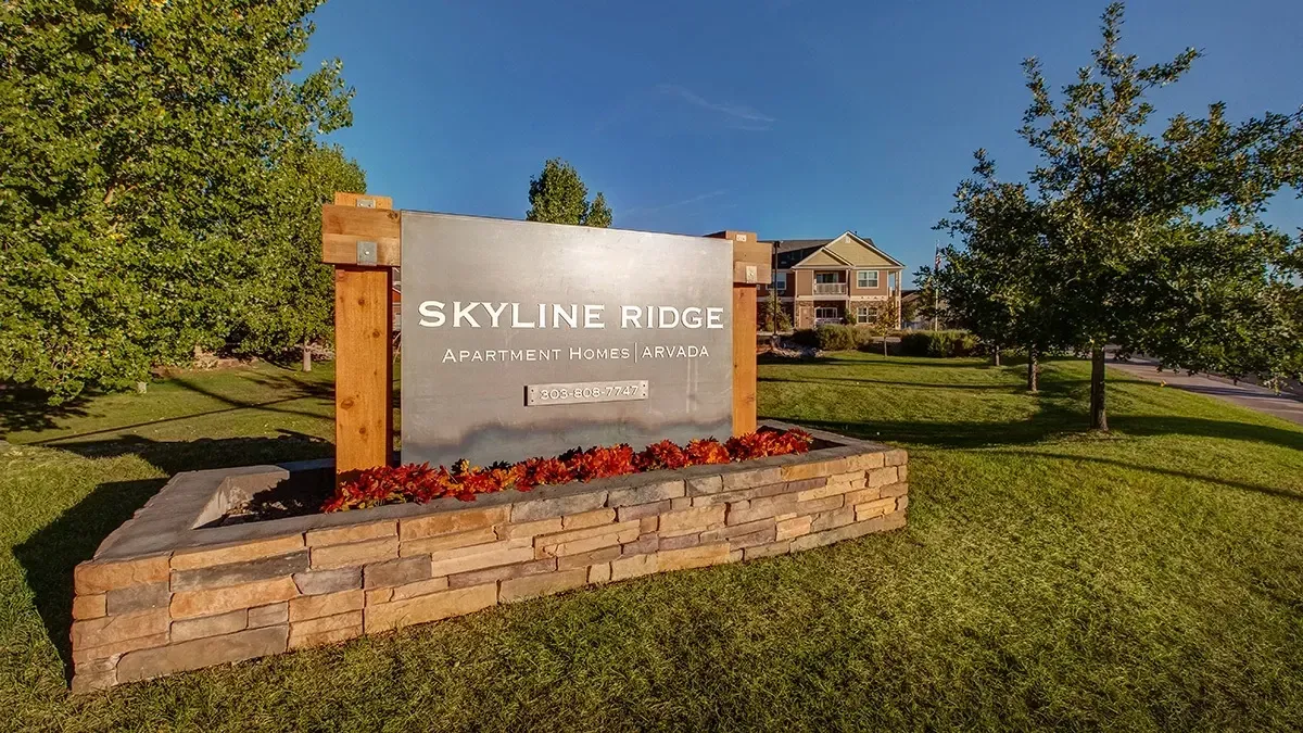Stone entrance sign reading “Skyline Ridge” beside a grassy lawn and trees in warm sunlight