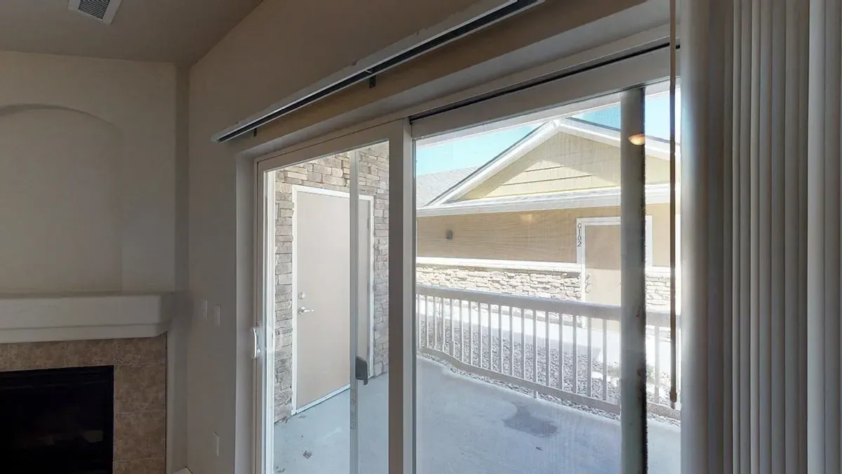 View through sliding glass door to an outdoor patio with a railing and a building beyond.