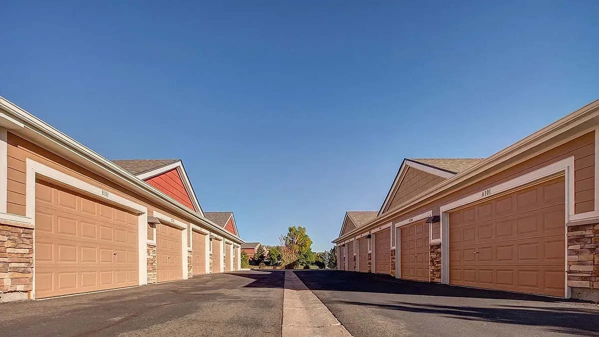 Sunlit row of tan brick garages lining both sides of a paved alley under a clear blue sky
