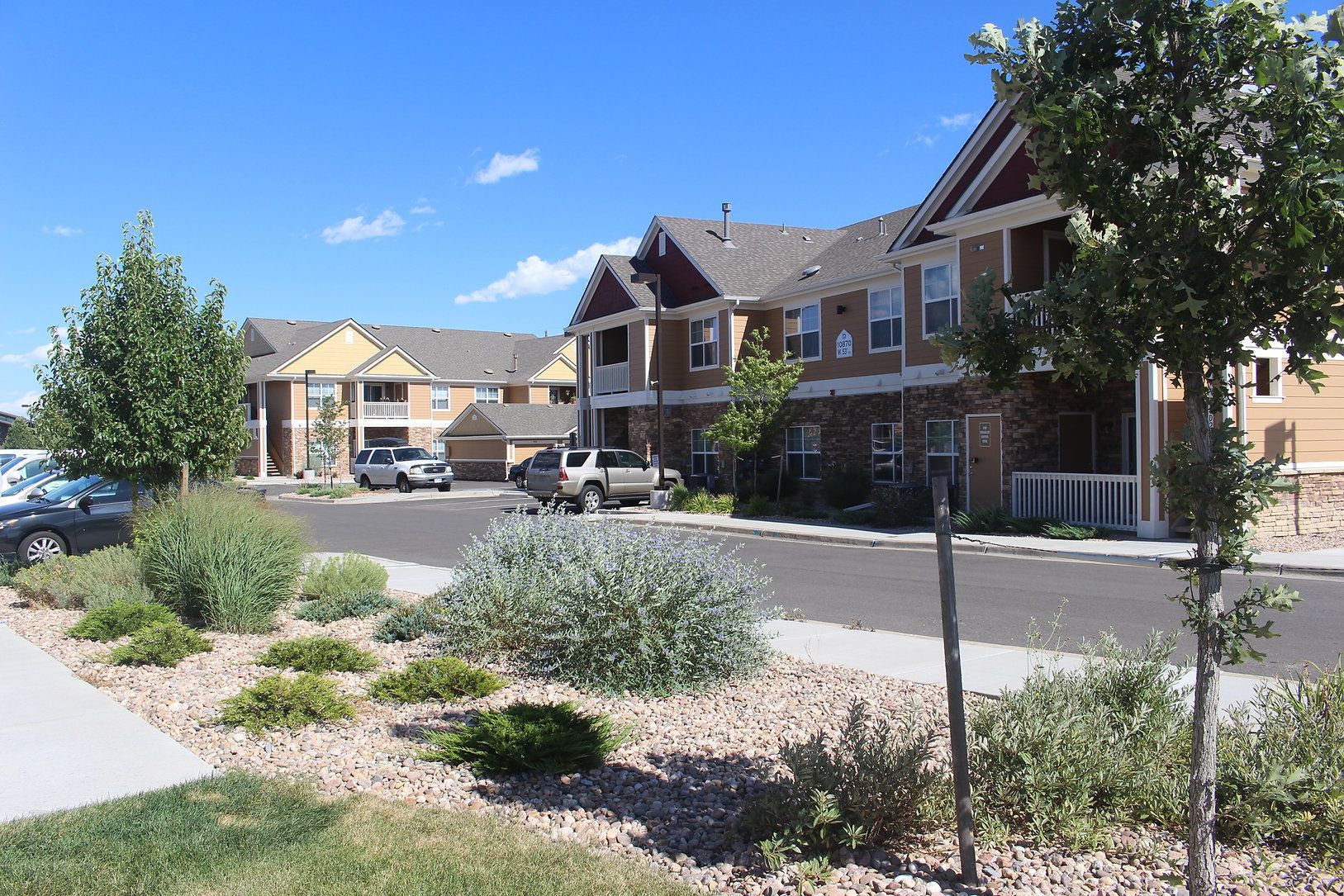 Landscaped apartment complex with brick buildings, parked cars, and blue sky
