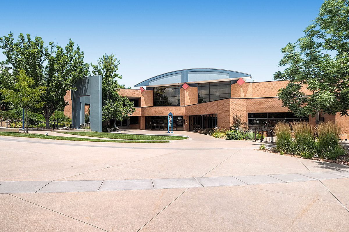 Brick building with glass roof, trees, and a wide paved driveway on a sunny day