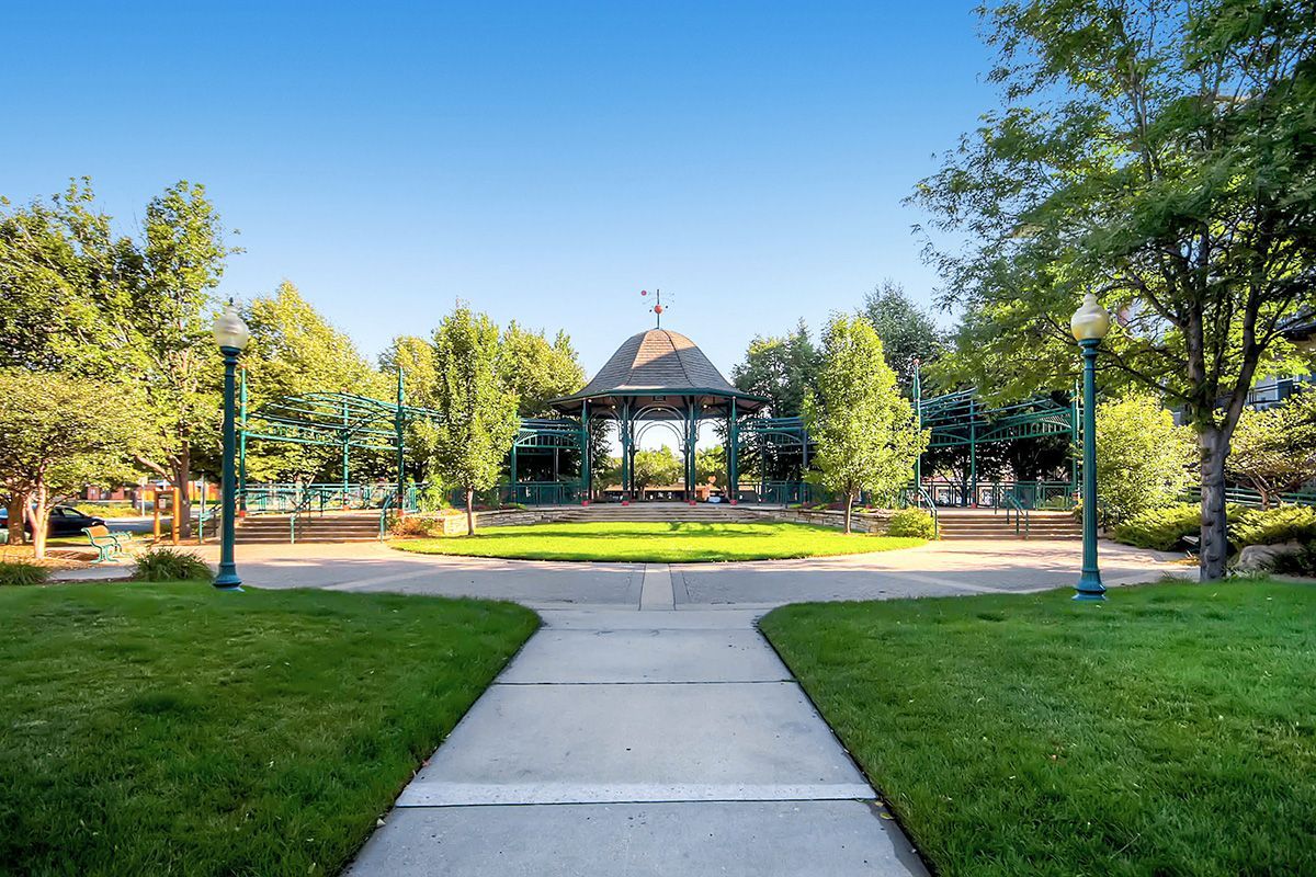 Sunny park walkway leading to a gazebo surrounded by trees and grass