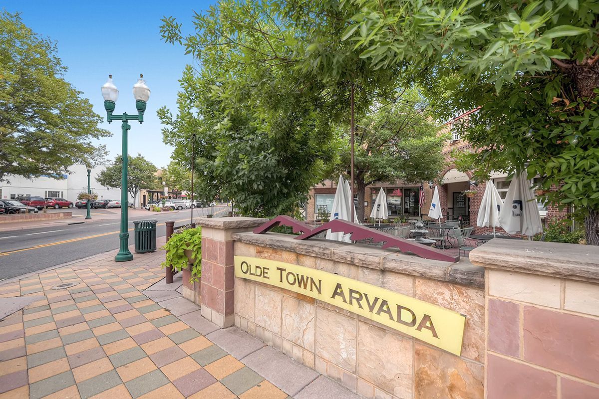 Old Town Arvada sign beside a tree-lined sidewalk and street lamps under a blue sky