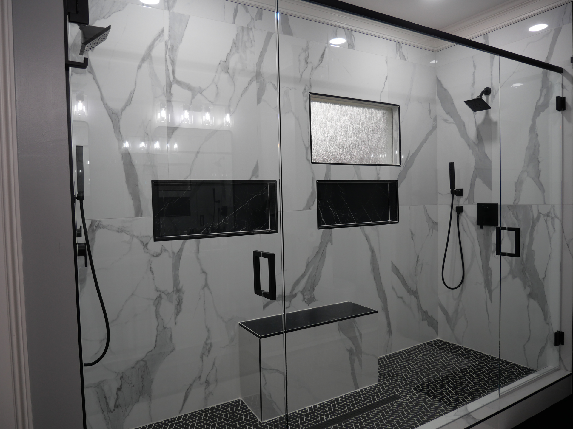 A walk in shower with a glass door and marble walls.