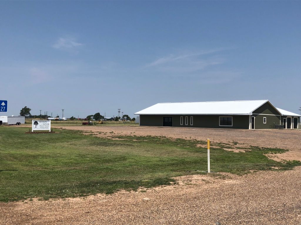 Single-story dark building with white roof in a grassy, open field under a clear sky.