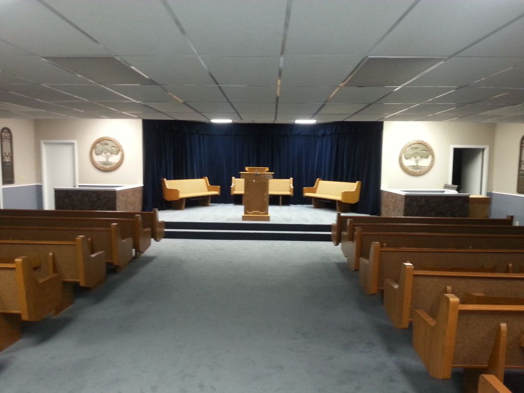 Empty courtroom with wooden benches, judge’s bench, and blue curtains behind the podium.