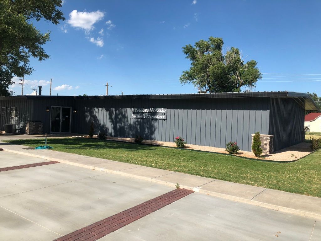 Single-story gray building with black trim beside a sidewalk under a clear blue sky.
