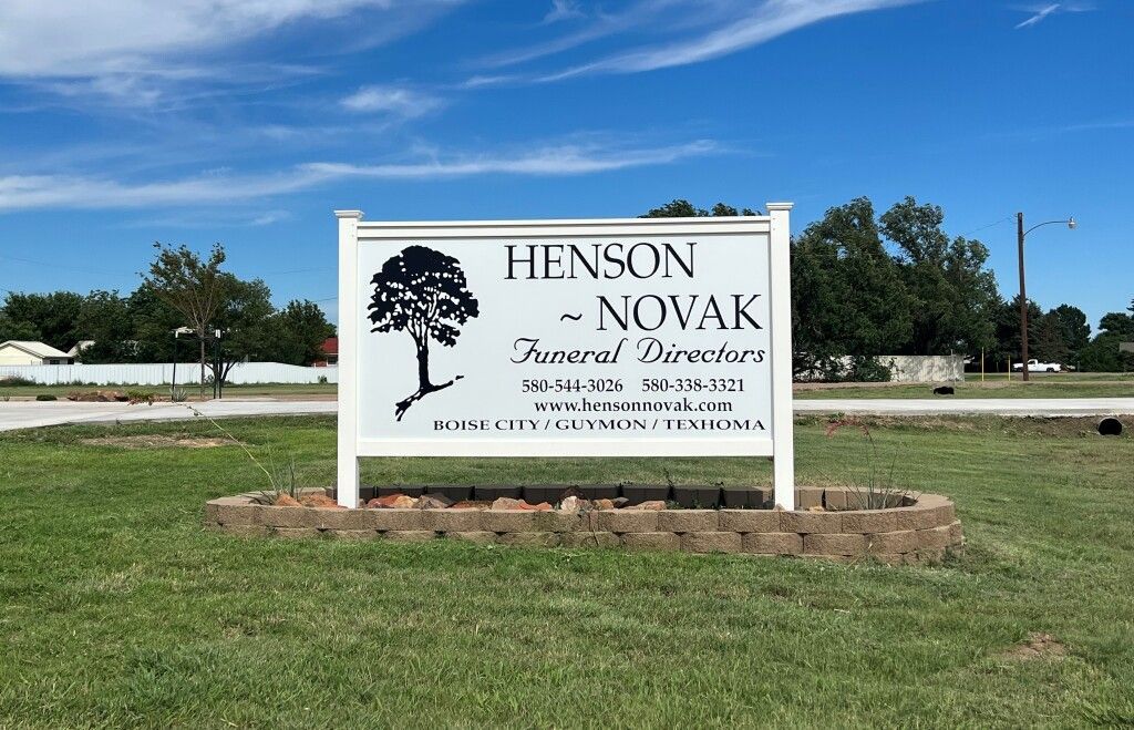 Tension-Novak funeral home sign with tree logo in a grassy lot under a blue sky