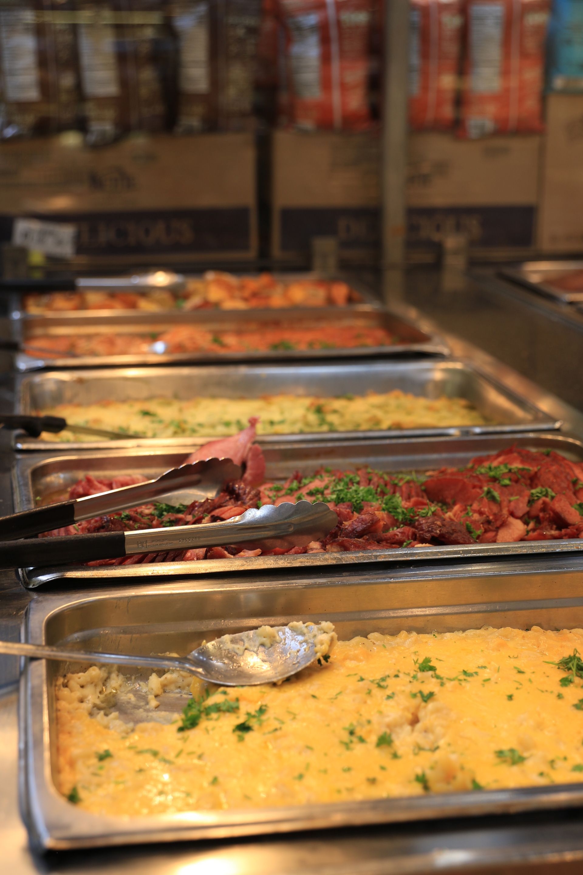 A display case at Lassens Kitchen filled with prepared salads and deli items, with shelves of bottled drinks below.