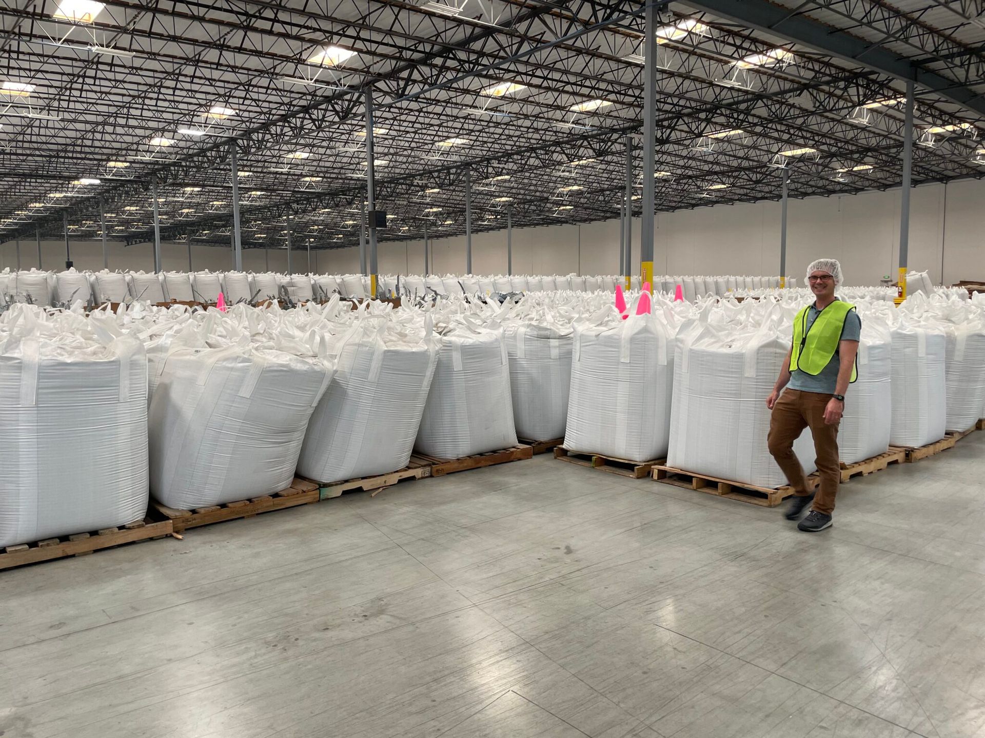 Man in vest stands by rows of large white bags in a warehouse.