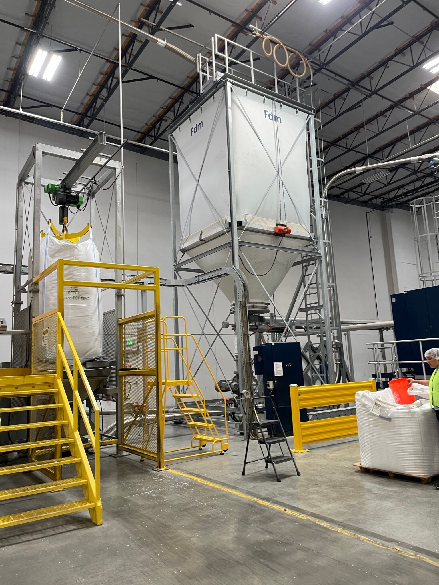 Industrial facility with large storage hoppers and a worker in a safety vest.