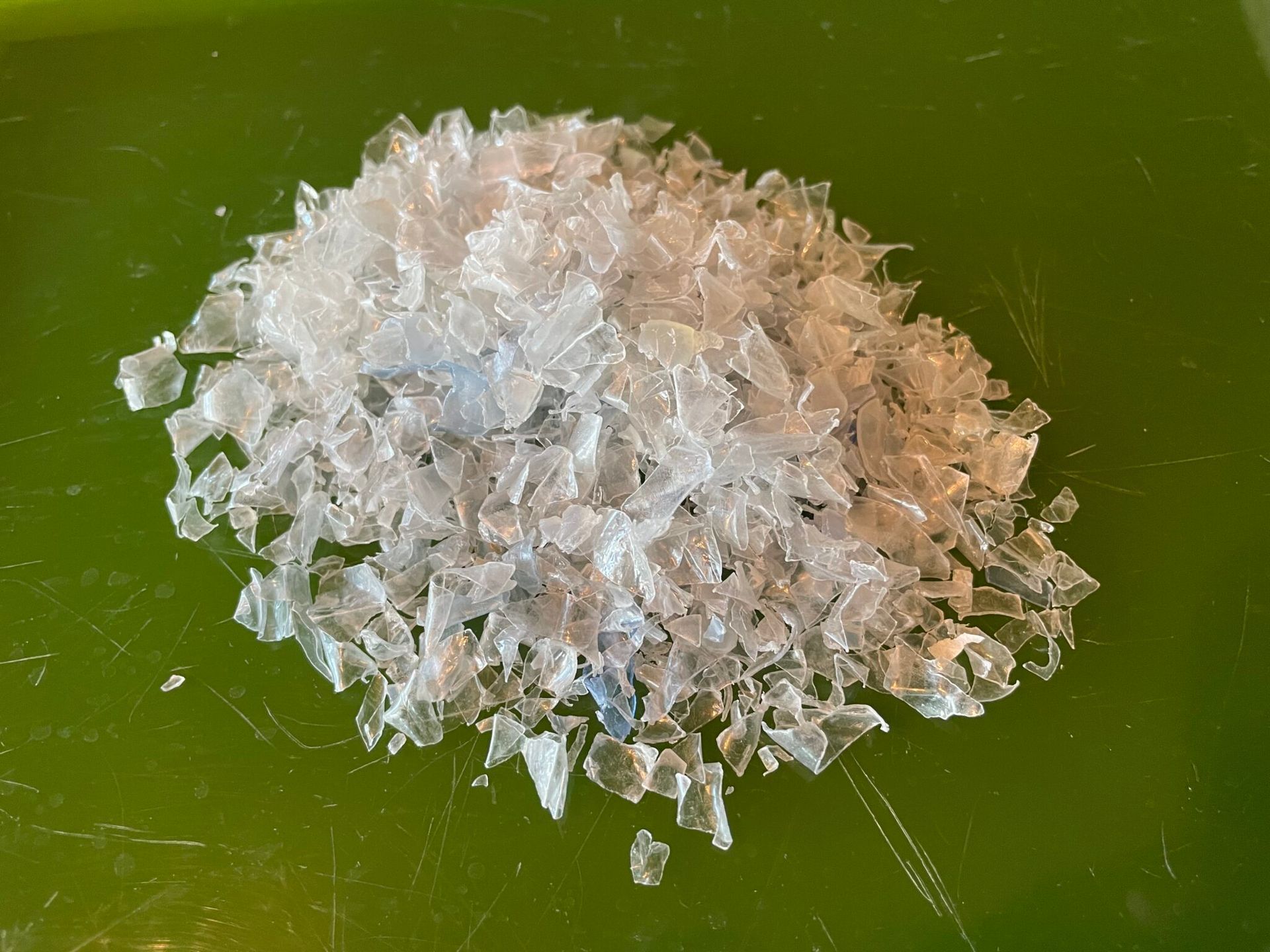 Pile of clear, shredded plastic flakes on a green cutting board.