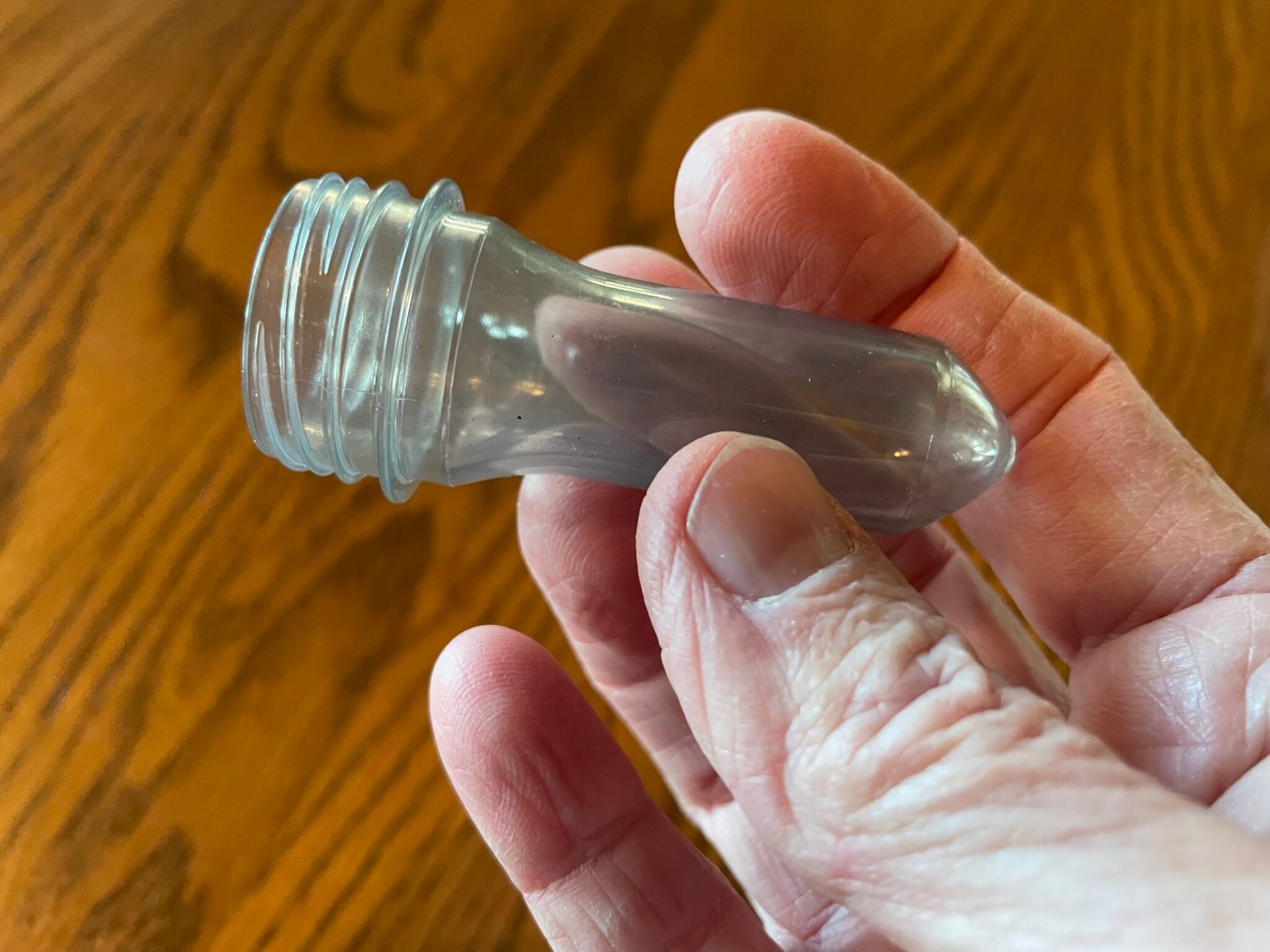 Hand holding a translucent, plastic bottle neck against a brown wooden surface.