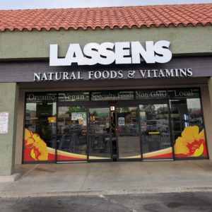 Storefront of a Lassens Natural Foods & Vitamins with green walls, orange tile roof, and glass doors with floral decals.