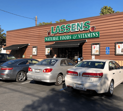 A Lassens Natural Foods and Vitamins storefront on a sunny day with cars parked in the foreground.