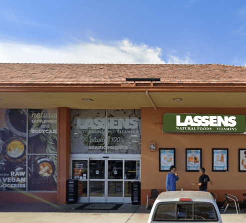 Lassens Natural Foods and Vitamins storefront with a tan facade, tile roof, and two people standing near the entrance.