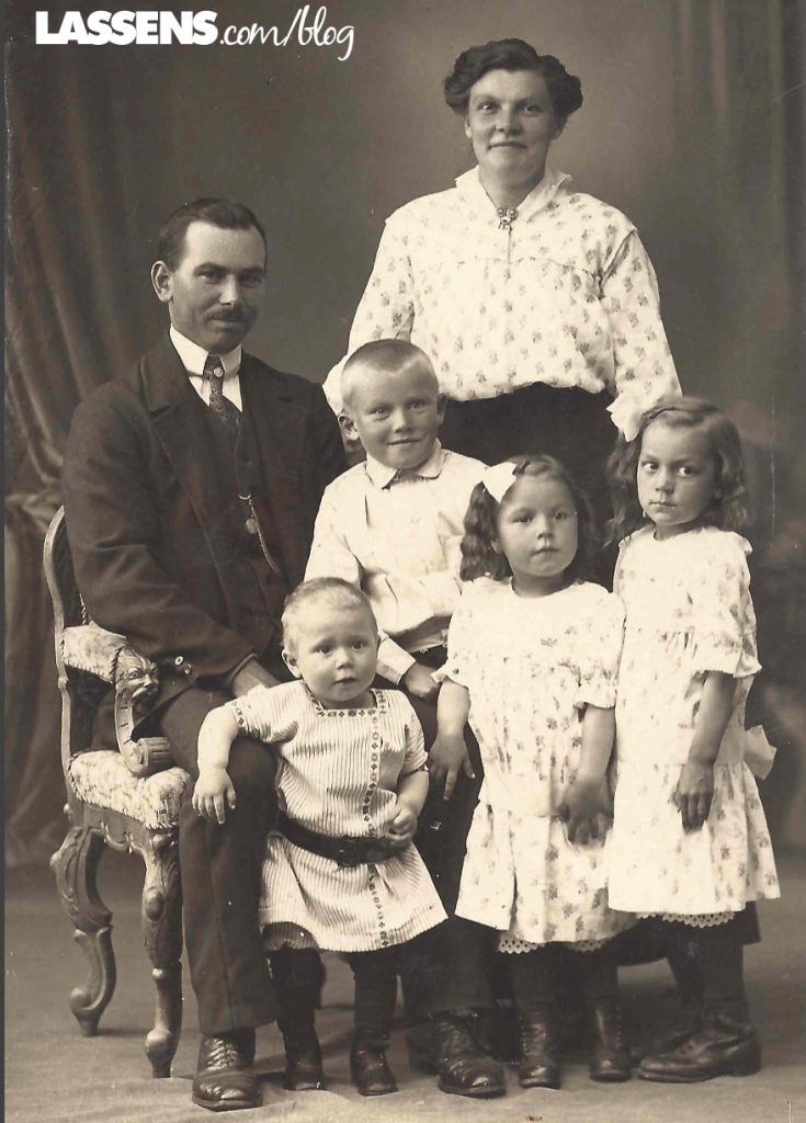 A formal sepia-toned studio portrait of a family of six, posed in a cluster against a draped backdrop.