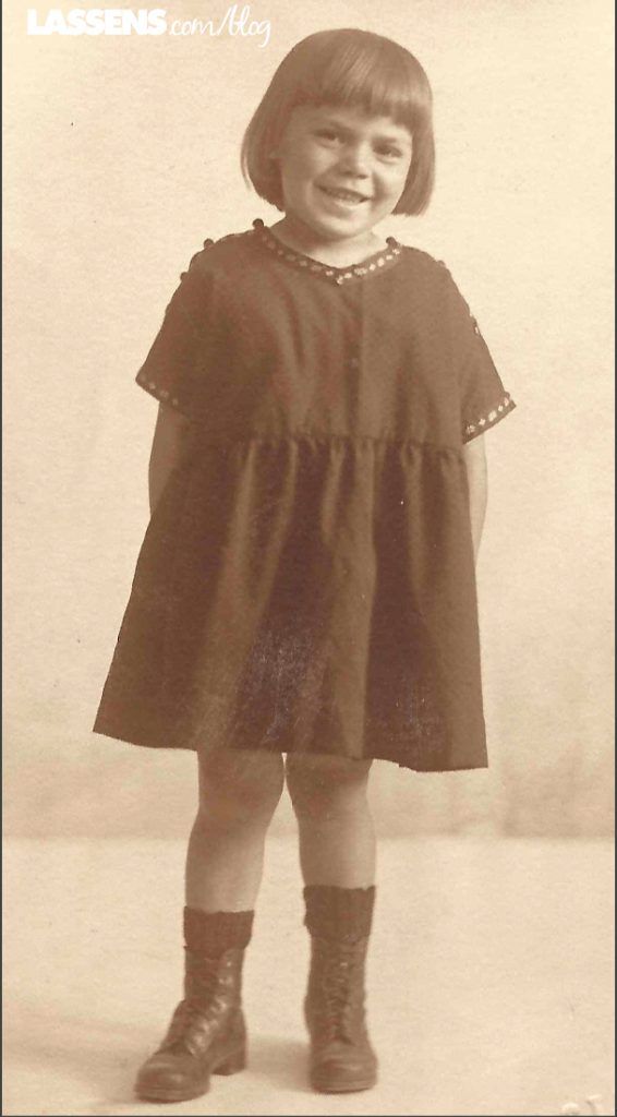 Young girl in dark dress and boots, smiling at the camera.