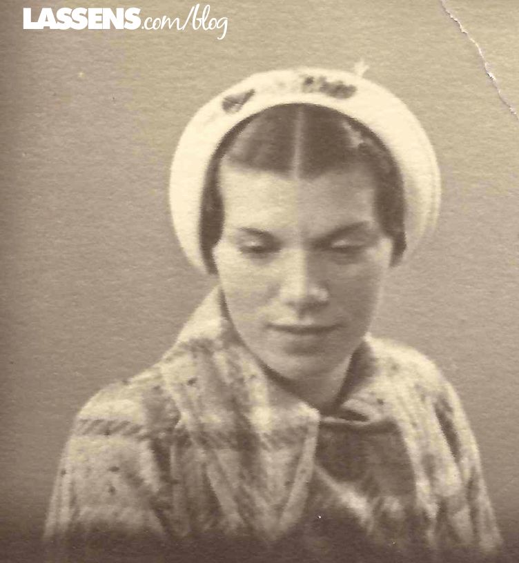 Woman in plaid coat and white hat, looking down.