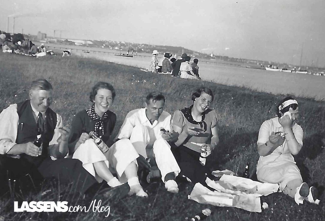 Five people picnicking on grassy hill overlooking a body of water and distant cityscape.