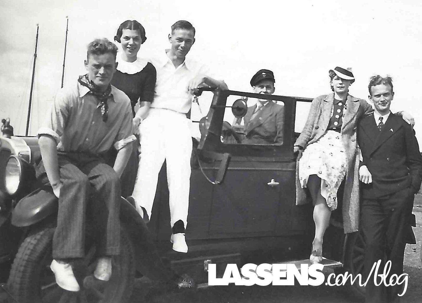 Group of people posing on and around a vintage car. Outdoors setting.