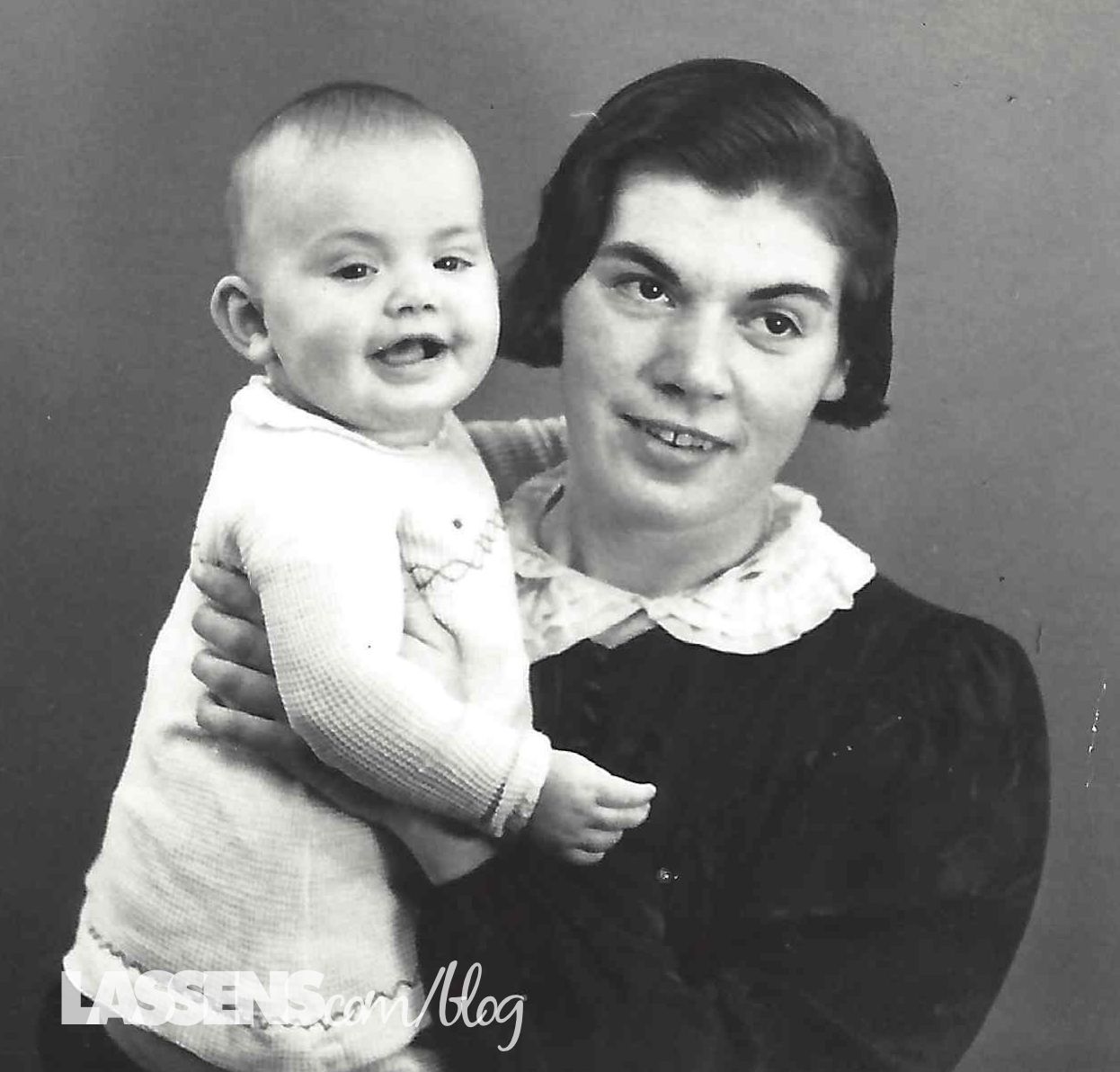 Woman holding a smiling baby; both are looking at the camera.