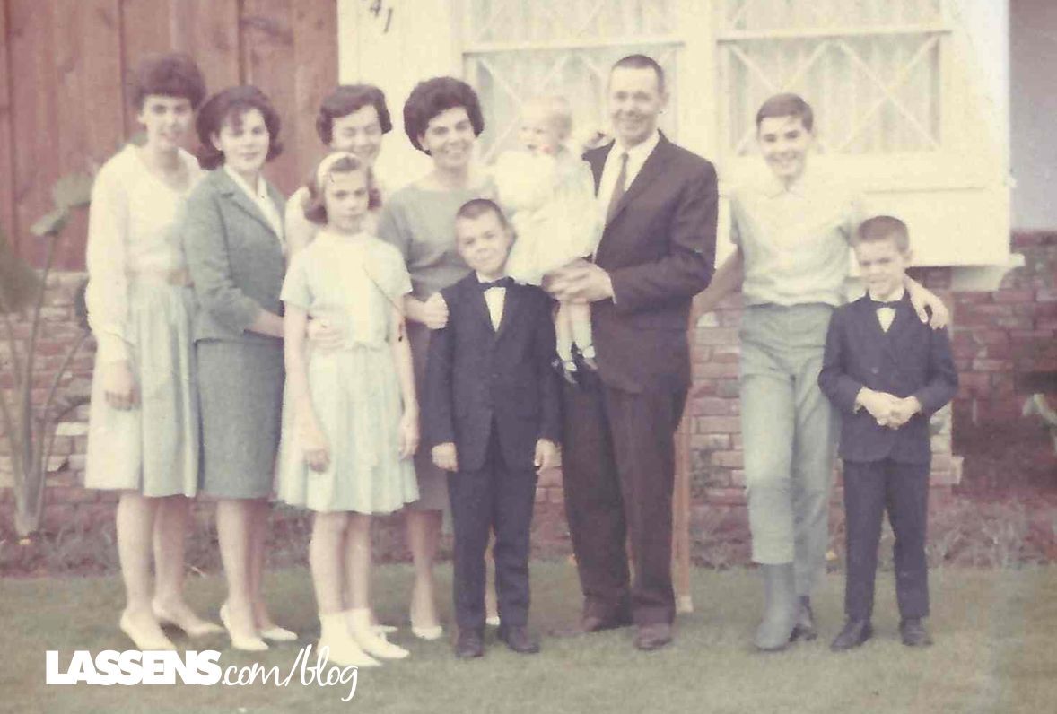 Family portrait outside a house. Nine people pose in formal attire, some smiling.