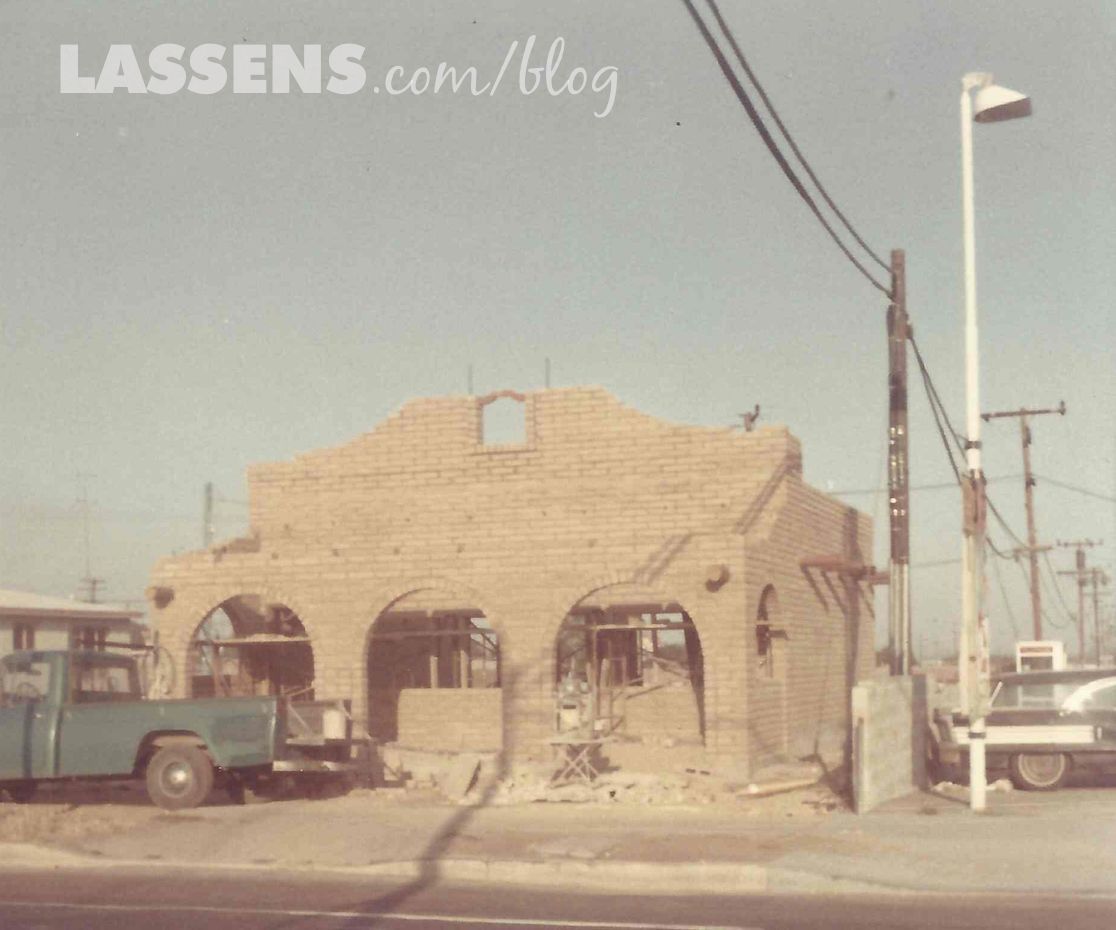 Building under construction, brick facade with arched openings. A green truck parked nearby. Sunny, outdoor setting.