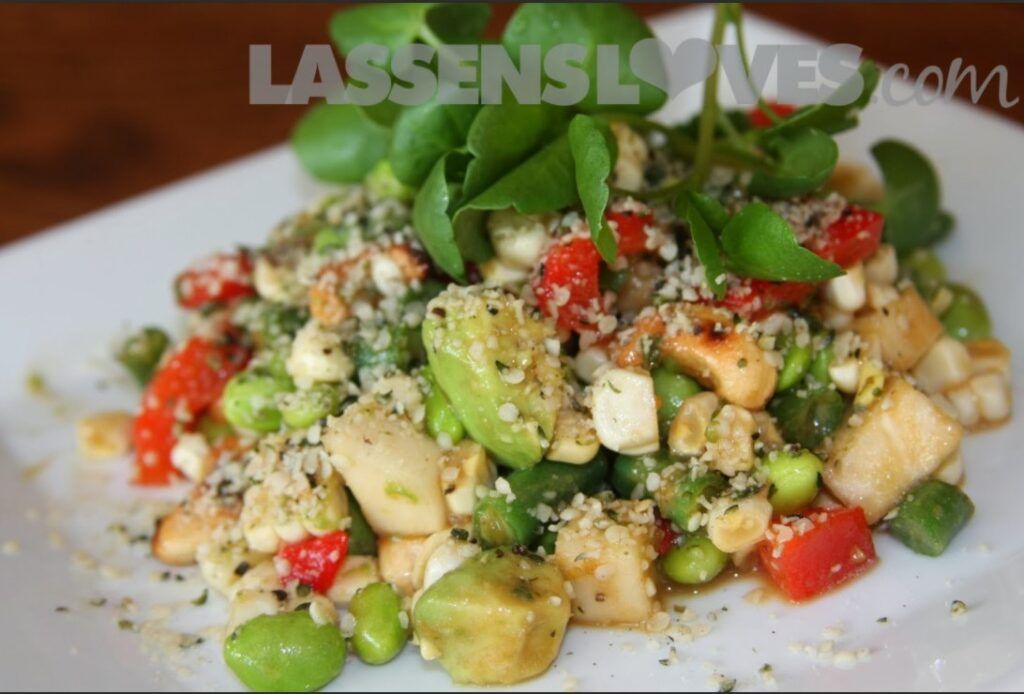 Salad with vegetables, avocado, and watercress on a white plate.