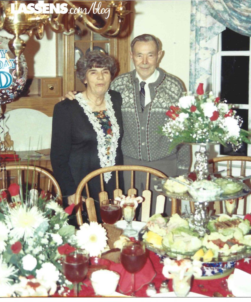 Couple poses by a table set for a celebration; flowers and food on display.