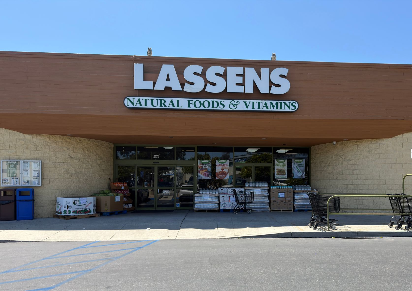 The storefront of Lassens Natural Foods & Vitamins with outdoor seating, a dark brown facade, and a green sign.