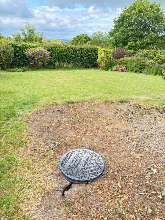 Concrete slab with rebar grid and level on top, framed by a raised border in a garden setting