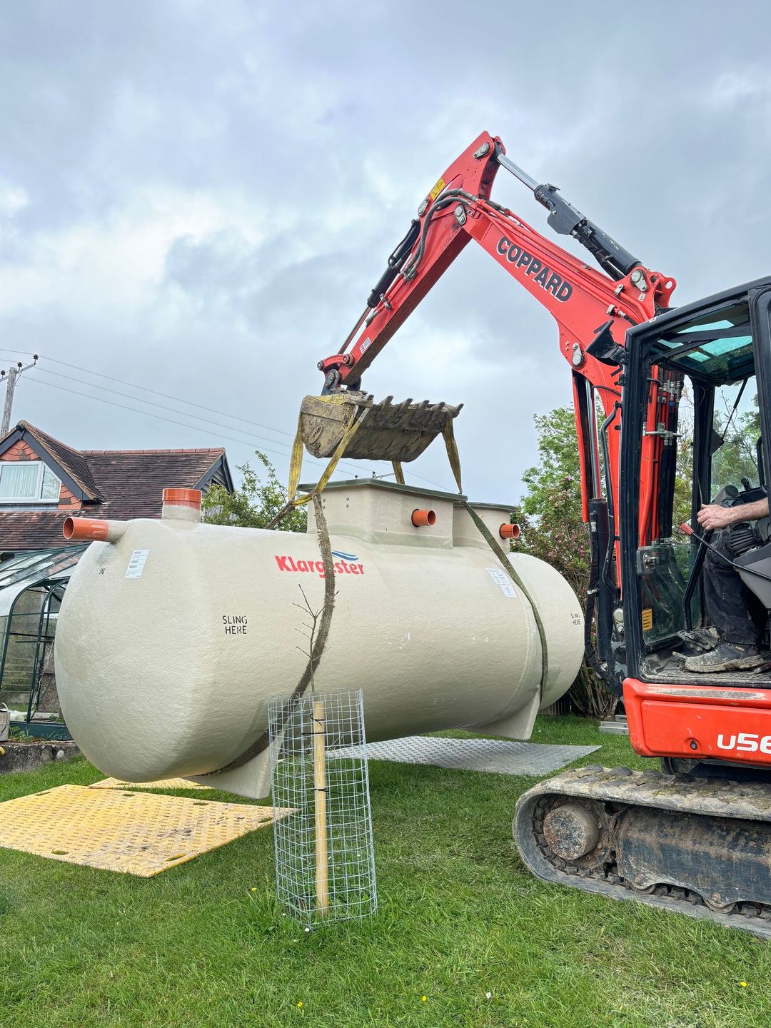 Construction crew guiding excavator placing concrete foundation walls at a suburban home site
