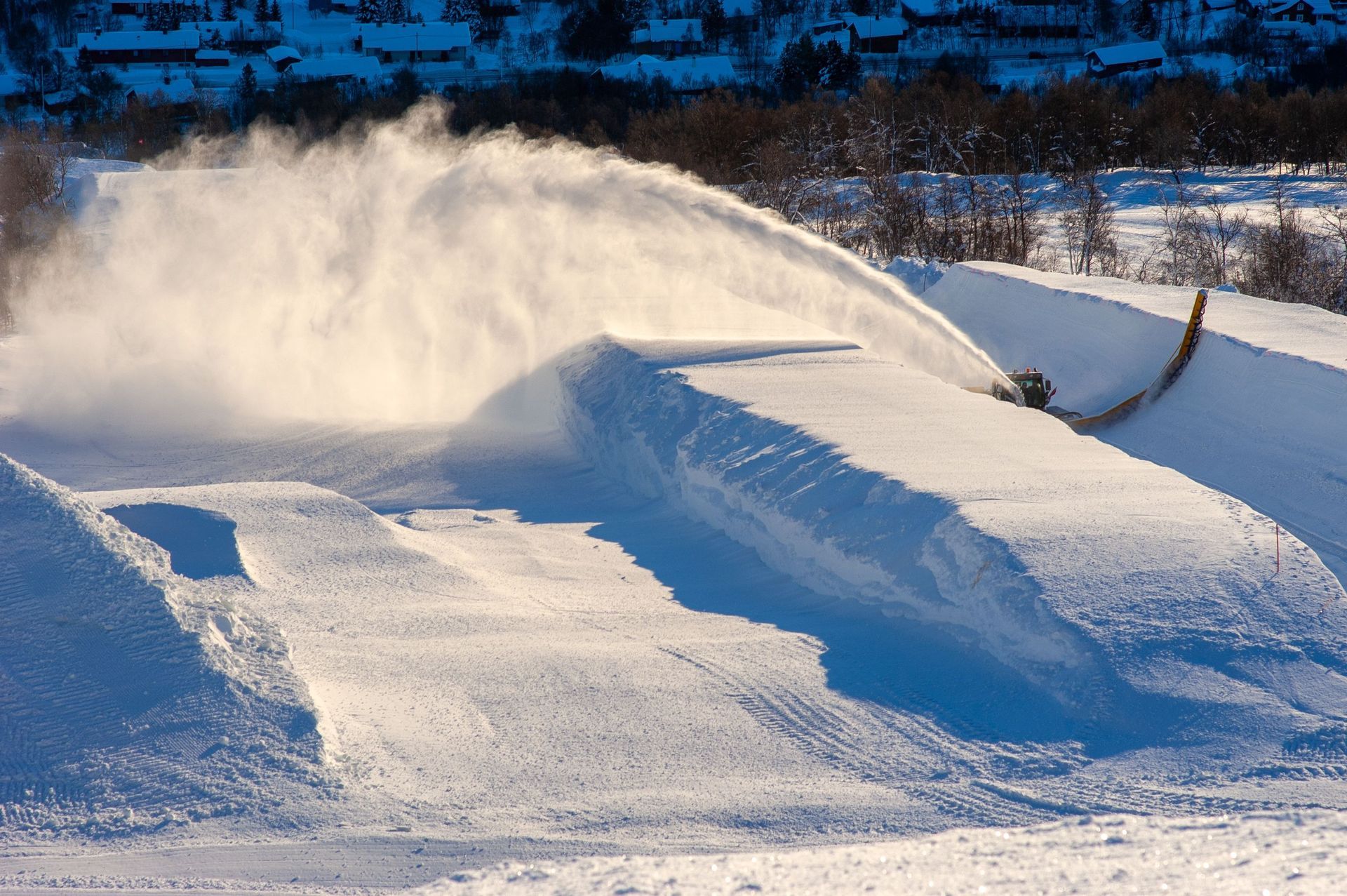 Snowmaking machine spraying white snow over a ski slope under a clear blue sky