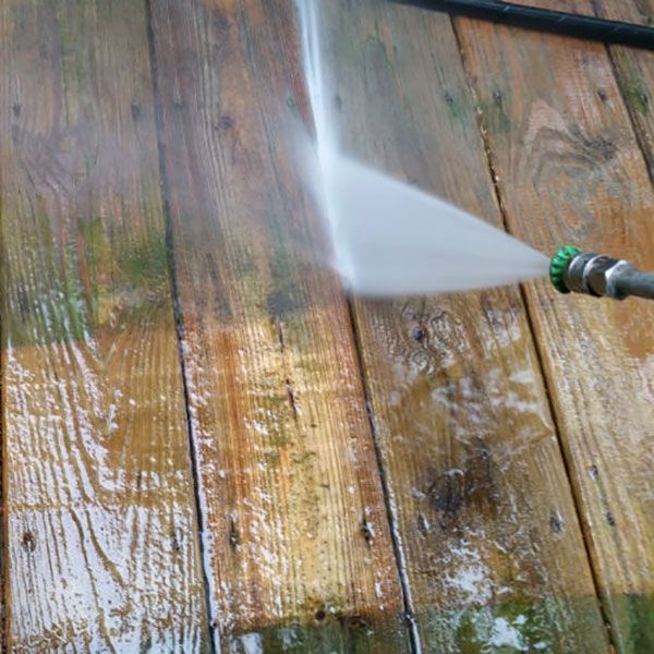 Power washer cleaning a weathered wooden deck; water spraying from the nozzle.