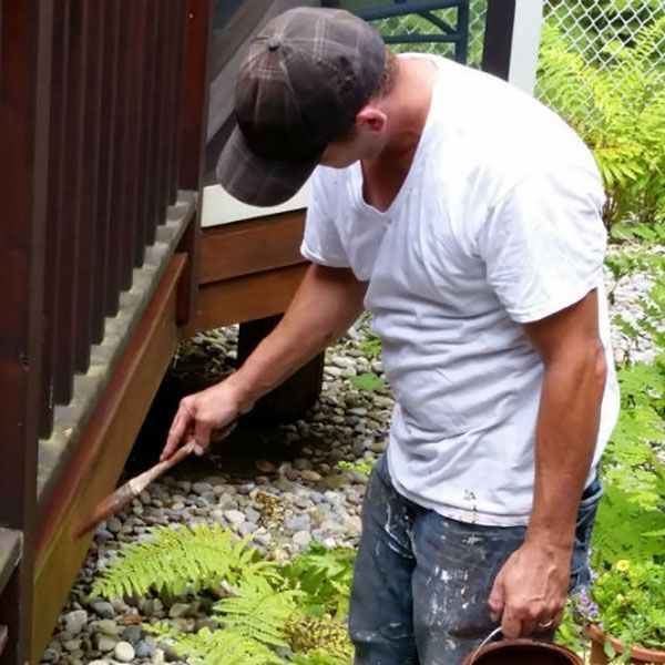 Man painting wooden structure outside with brush and bucket.