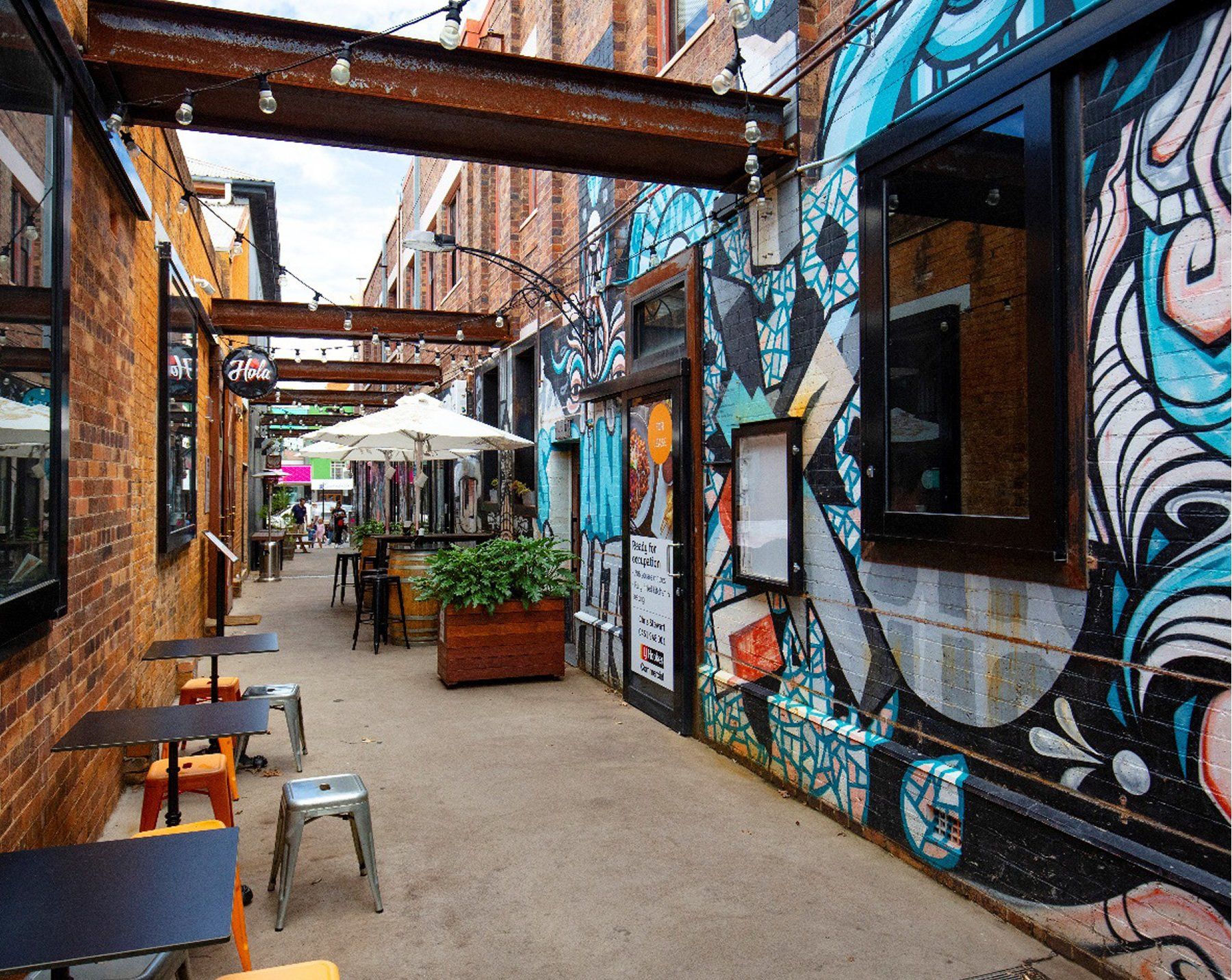 A narrow alleyway between two buildings with tables and chairs and graffiti on the walls.
