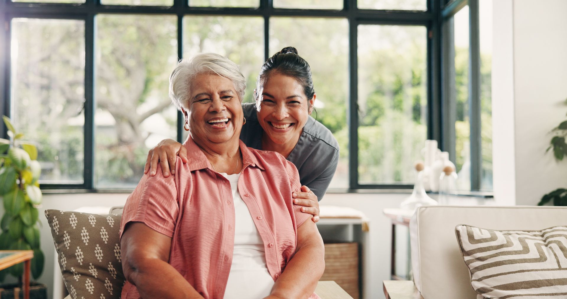 Smiling woman embracing an older woman in a bright living room with large windows